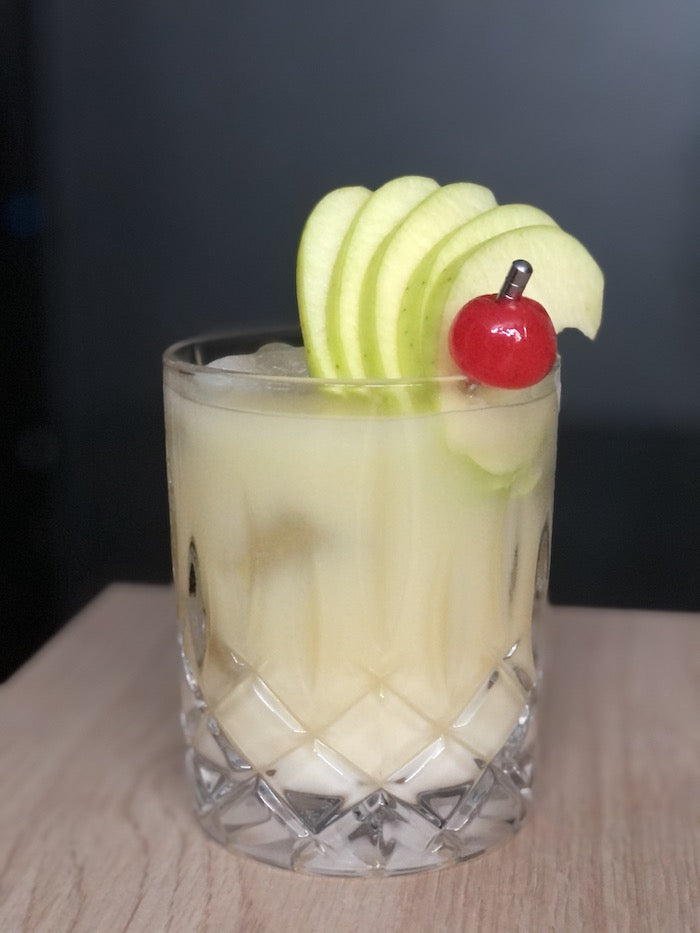 Cremiger Orangen-Apfel-Batida Cocktail im Tumblerglas mit Apfelscheiben und Cocktailkirsche als Garnitur.