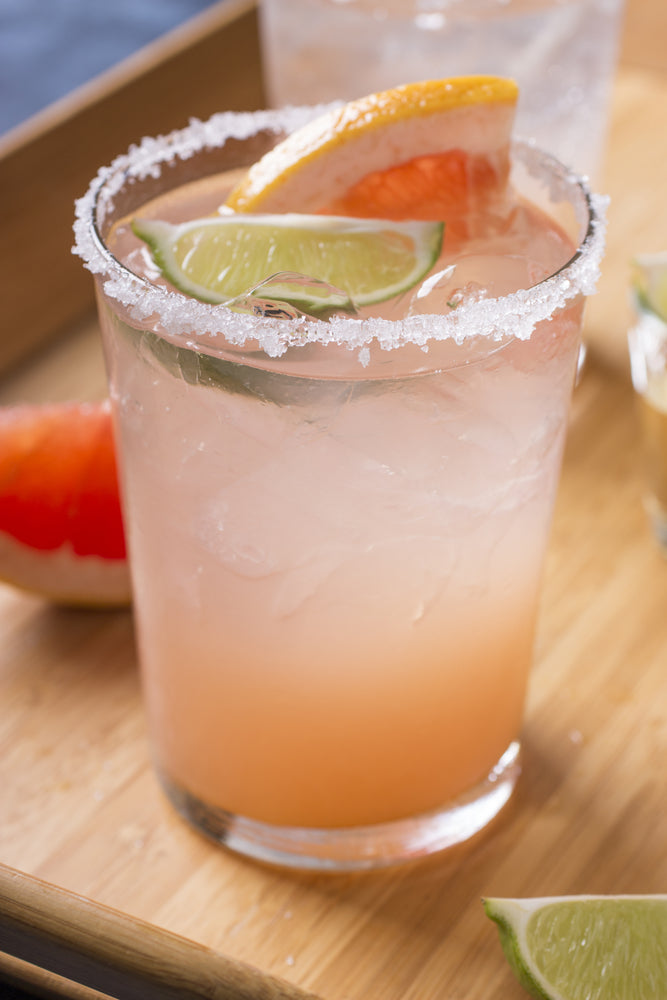 Paloma Cocktail im Glas mit Salzrand, Limetten- und Grapefruitscheibe auf Holzbrett