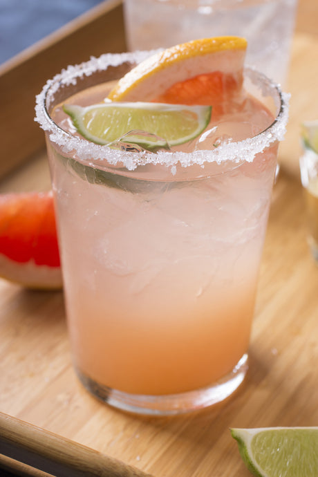 Paloma Cocktail im Glas mit Salzrand, Limetten- und Grapefruitscheibe auf Holzbrett