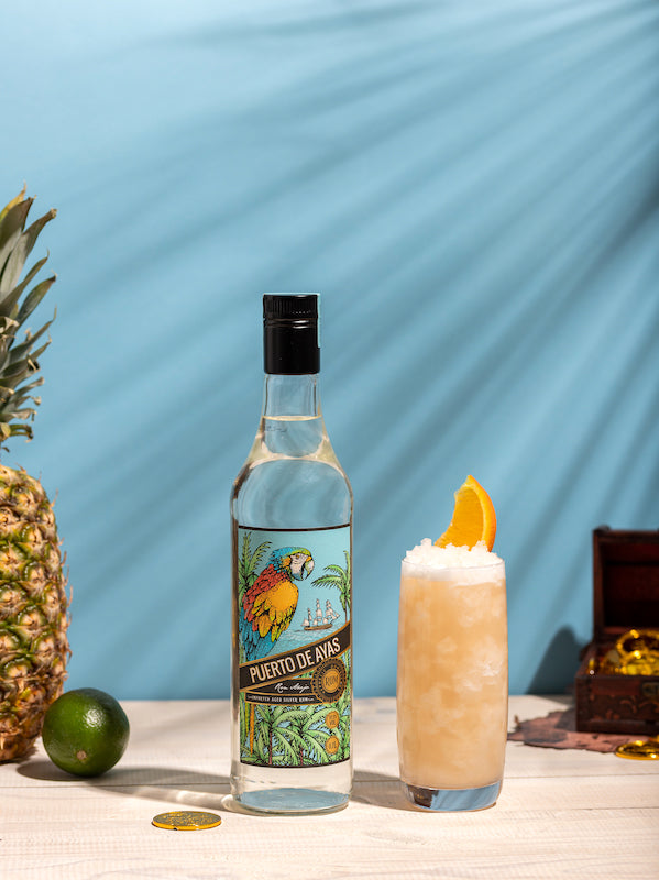 Tropischer Papa Doble Cocktail mit Crushed Ice und Orangenscheibe neben einer Rumflasche mit Papagei-Design.