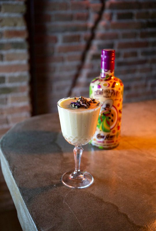 Cocktail Passion Nº5 mit Maracuja-Tequila, serviert im Glas auf Bartheke mit Lupita Pasion Likör im Hintergrund.