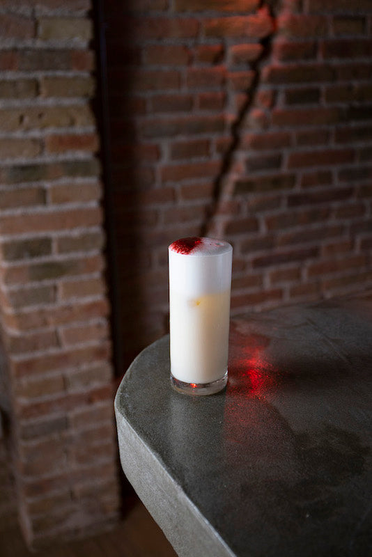 Passion Sour im Tall Glas mit weißer Schaumschicht und Erdbeerbonbon-Topping auf Steintisch