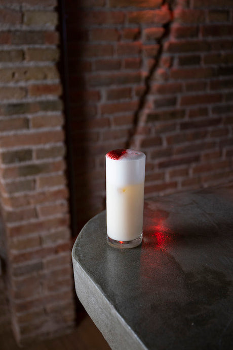 Passion Sour im Tall Glas mit weißer Schaumschicht und Erdbeerbonbon-Topping auf Steintisch