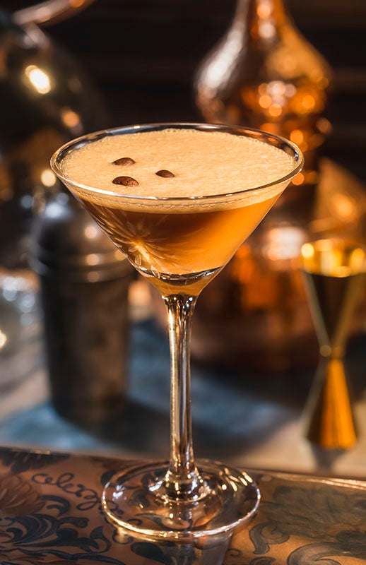 Portos Martini Cocktail in einem Cocktailglas mit drei Kaffeebohnen als Dekoration, im Hintergrund Barutensilien.