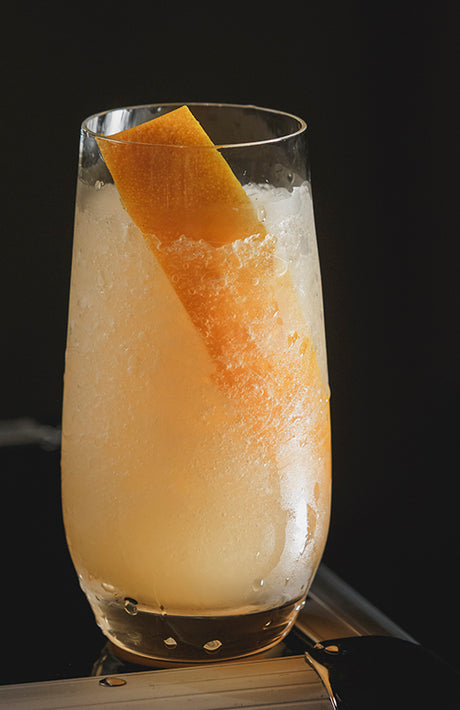 Rawaki Cocktail im Highball-Glas mit Crushed Ice und Orangenzeste vor dunklem Hintergrund