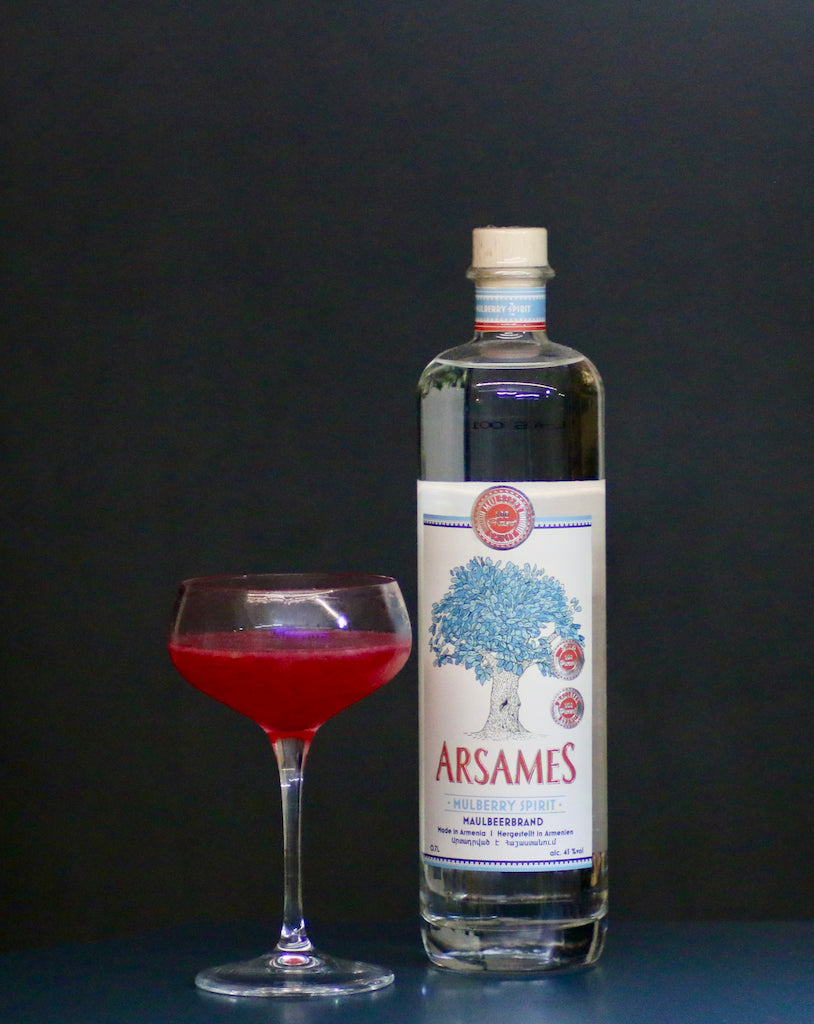 Red Dreams Cocktail mit Arsames Maulbeerbrand Flasche und rotem Drink in Coupette vor dunklem Hintergrund