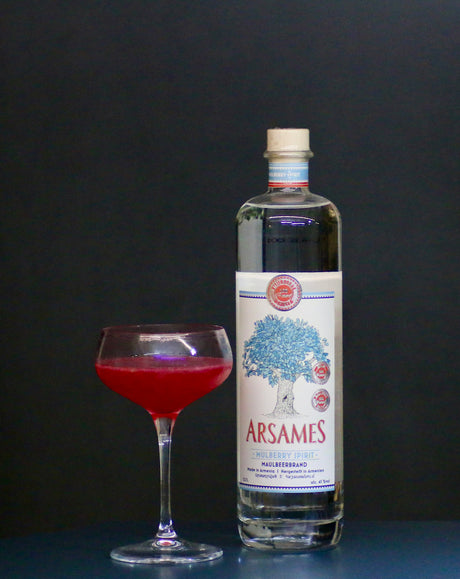 Red Dreams Cocktail mit Arsames Maulbeerbrand Flasche und rotem Drink in Coupette vor dunklem Hintergrund