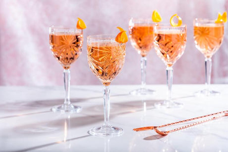 Salcombe Rosé Spritz Cocktails in Weingläsern mit Orangenzesten auf hellem Tisch