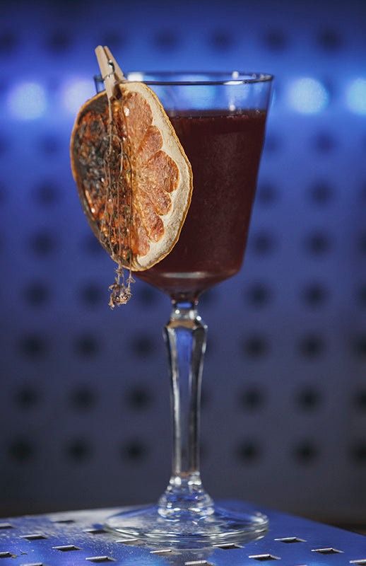 Sangria Sunset Cocktail im Weinglas mit getrockneter Orangenscheibe vor blauem Barhintergrund