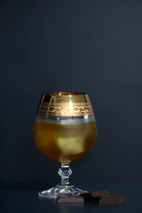 Sol y Sombra Cocktail im verzierten Glas mit Eis und Schokolade vor dunklem Hintergrund