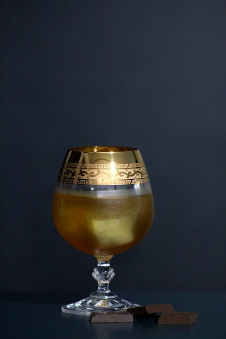 Sol y Sombra Cocktail im verzierten Glas mit Eis und Schokolade vor dunklem Hintergrund
