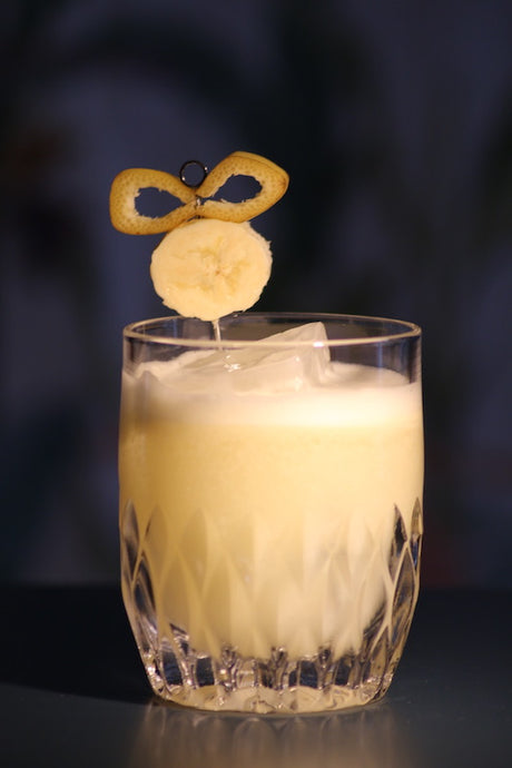 Somewhere in South America Cocktail mit Banane und Orangenzeste im Tumbler vor dunklem Hintergrund