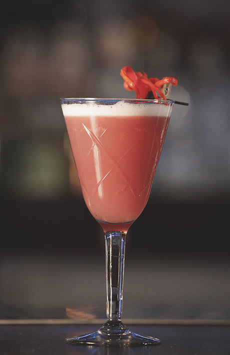 Sour Thai Jasley Cocktail im Cocktailglas mit Schaumschicht und roter Dekoration auf Bar vor unscharfem Hintergrund