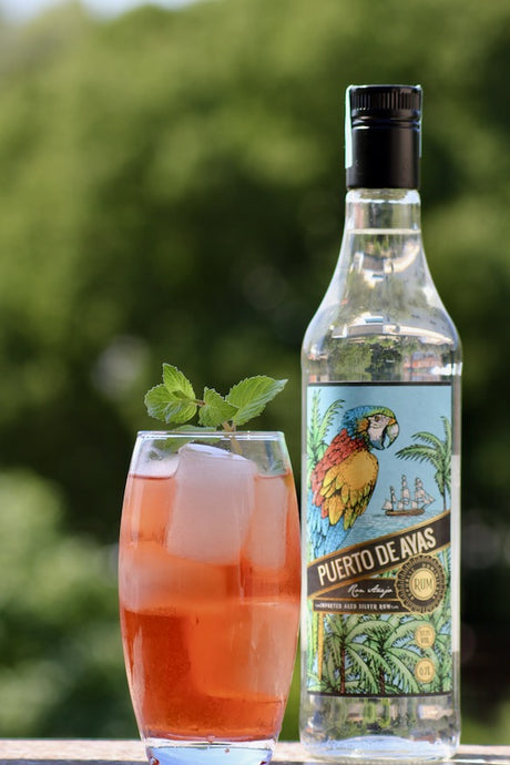 Surf Rider Cocktail mit Minze und Eis neben Puerto de Ayas Rum Flasche vor grünem Hintergrund