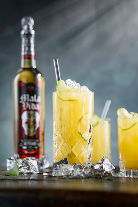 Tequila Ananas Punch im Highball Glas mit Eis und Limette, dahinter Tequila Flasche auf dunklem Hintergrund