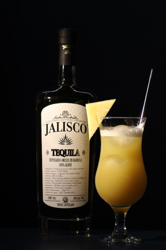Tequila Matador Cocktail mit Ananasstück und Jalisco Tequila Flasche vor dunklem Hintergrund