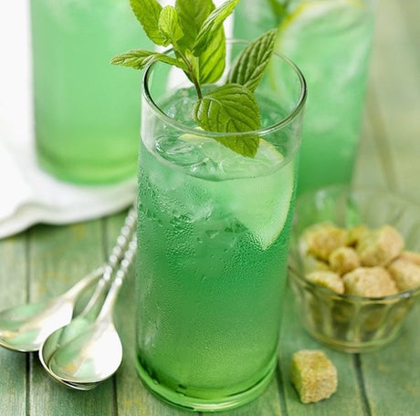 Green Beast Cocktail in einem hohen Glas mit Eiswürfeln, Limettenscheibe und Minzzweig, daneben brauner Zucker.