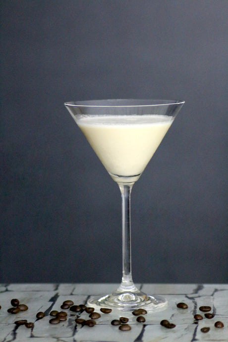 Toasted Almond Cocktail im Martiniglas auf Tisch mit Kaffeebohnen vor grauem Hintergrund