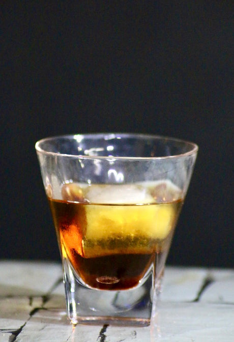 Toro Bravo Cocktail im Tumblerglas mit zweifarbiger Schichtung auf Tisch vor dunklem Hintergrund