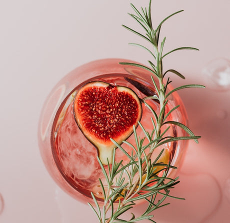 Violet'prov Cocktail mit Feige und Rosmarin im Glas, rosa Drink mit Eis von oben fotografiert