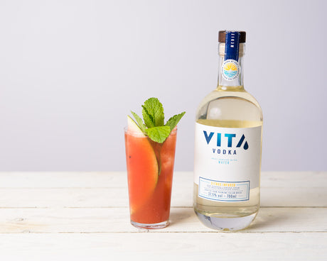 Vita Refresher Cocktail mit Vita Vodka Citrus, Wassermelone und Minze auf weißem Holztisch.