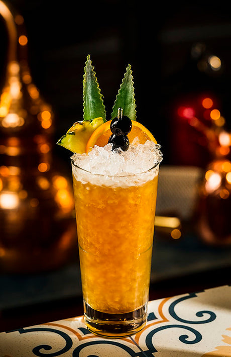 Wermut Ananas Cobbler Cocktail im Highball-Glas mit Crushed Ice, Ananas, Orange und Kirsche dekoriert