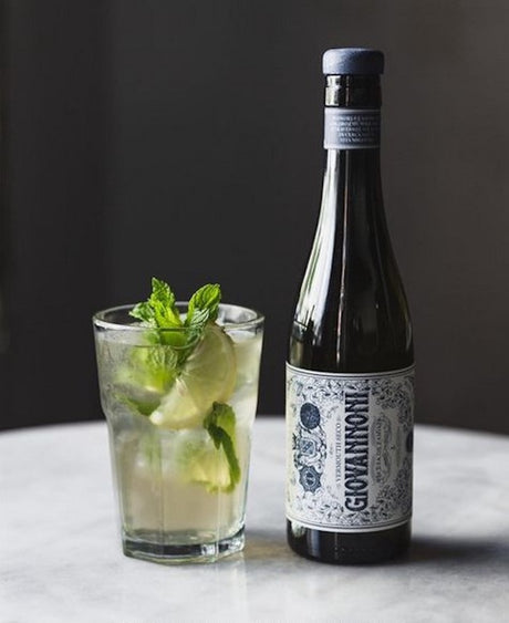 Mentolada Cocktail im Highball Glas mit Limette und Minze neben Giovannoni Seco Wermut Flasche