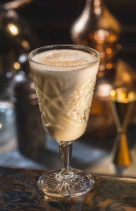 White Chocolate Milk Punch in einem verzierten Glas mit cremiger Textur, dekoriert mit einer feinen Prise Muskat.