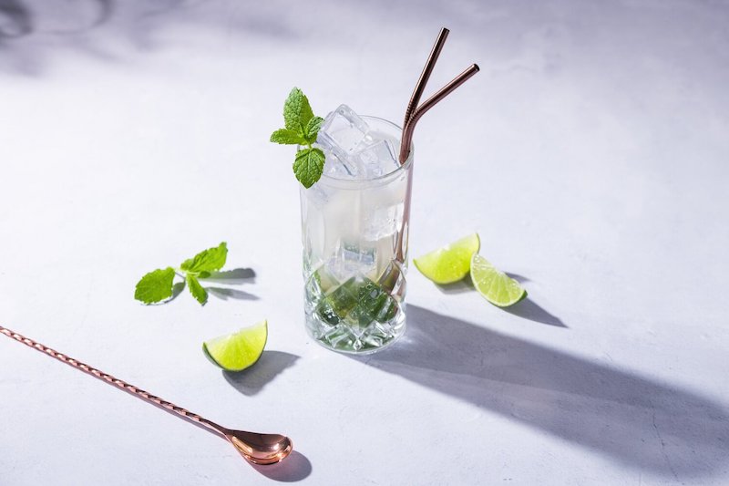 Whitestrand Spiced Rum Mojito Cocktail im Highball-Glas, garniert mit frischer Minze und Limetten auf einem hellen Tisch.