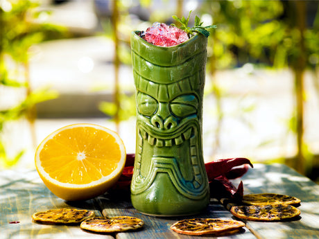 Zombie Cocktail im grünen Tiki-Becher mit Crushed Ice, Minze und Zitrusfrüchten, dekoriert mit getrockneten Orangenscheiben