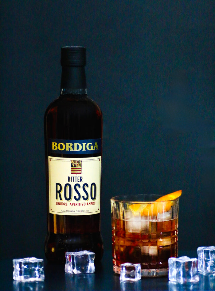 Bordiga Bitter Rosso-Flasche neben einem Amaretto Negroni im Rocks-Glas mit Eiswürfeln und Orangenzeste.