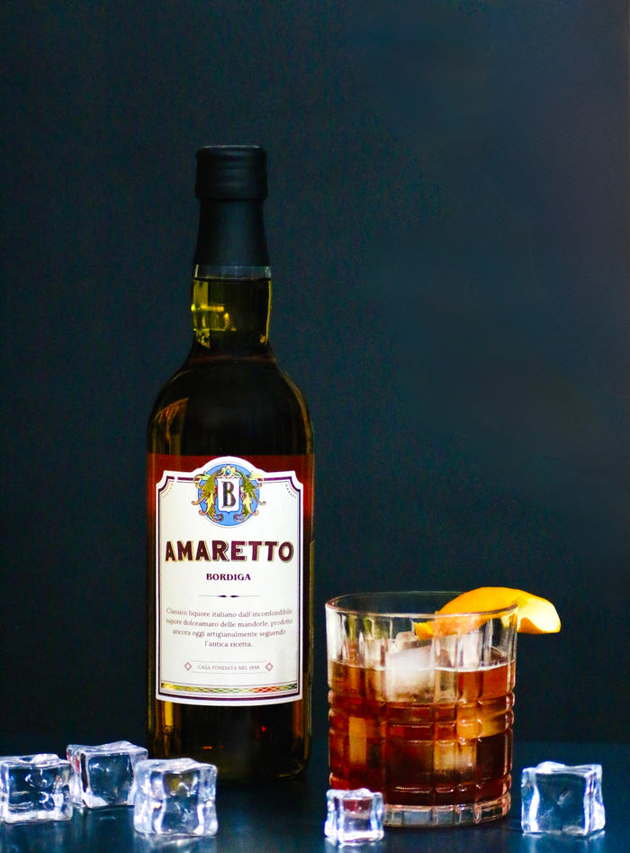 Bordiga Amaretto-Flasche neben einem Amaretto Negroni im Rocks-Glas mit Eiswürfeln und Orangenzeste.