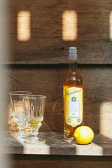 Flasche Aqualanca L'Anis d'Antan mit zwei Gläsern und einer Zitrone auf einem Holztisch