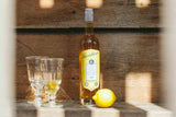 Flasche Aqualanca L'Anis d'Antan mit zwei Gläsern und einer Zitrone auf einem Holztisch im Sonnenlicht