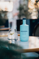 Arduenna No Alcohol 0,5 l neben einem Glas mit Tonic, Eis und Limette auf einem runden Tisch mit unscharfem Hintergrund