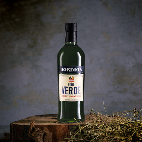 Flasche Bordiga Bitter Verde auf rustikalem Holzstumpf, umgeben von natürlichen Kräutern vor einem dunklen Hintergrund.
