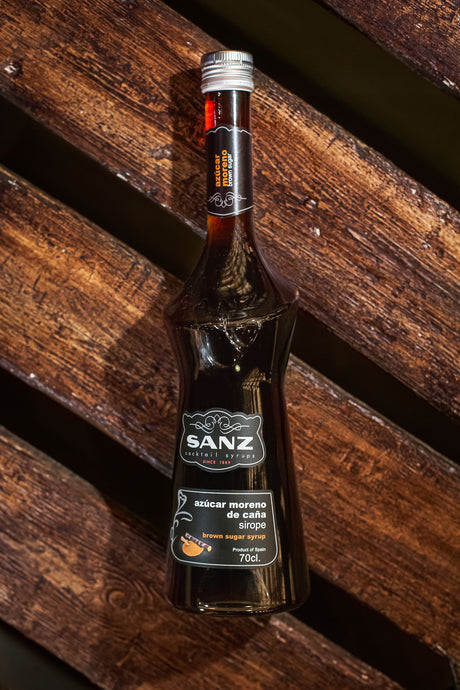 Brauner Rohrzuckersirup Sanz in einer dunklen Flasche auf rustikalem Holzuntergrund, Etikett mit 70 cl-Angabe sichtbar.