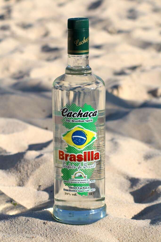 Cachaça Brasilla Flasche im Sand, mit Sonnenlicht und Schatten auf unebenem Untergrund.