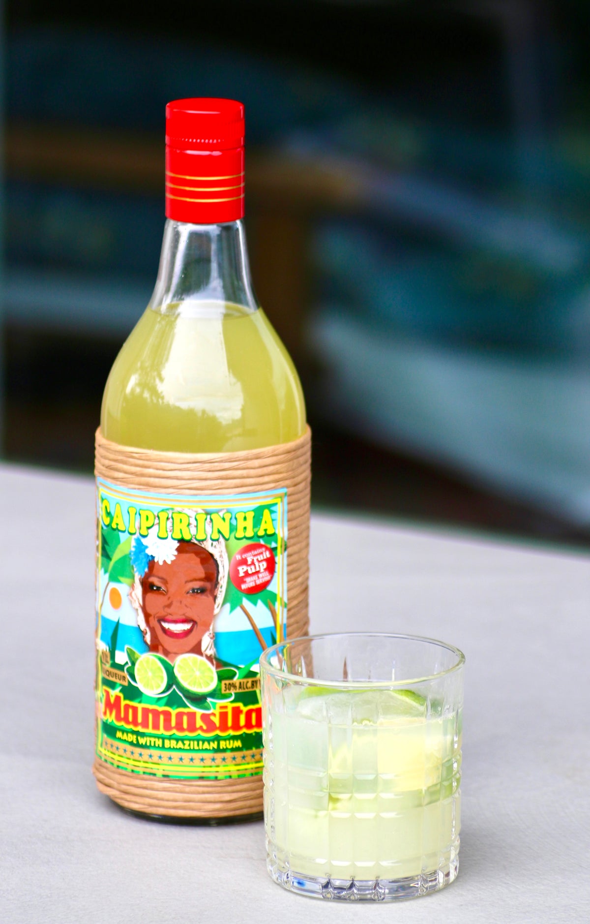 Mamasita Caipirinha Mix Flasche mit serviertem Caipirinha im Glas auf hellem Tisch