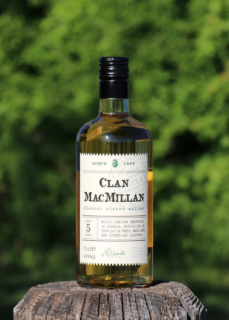 Flasche Clan MacMillan Scotch Whisky, 5 Jahre gereift, auf Holz mit Naturhintergrund, Etikett in Weiß mit schwarzer Schrift.
