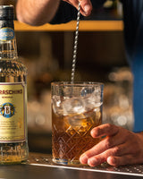 Zubereitung eines Cocktails mit Eis und Rührstab neben einer Flasche Maraschino Bordiga an einer Bar.