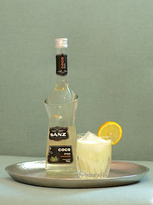 Coconut Virgin Sour Cocktail mit Kokossirup Flasche und Glas mit Eis und Zitronenscheibe auf Tablett