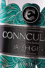 Nahaufnahme des Conncullin Irish Gin Etiketts mit silbernem Schriftzug, türkisfarbenen Wellen und schwarzem Emblem der Connacht Distillery.