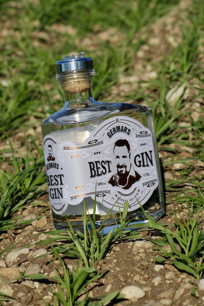Germar's Best Gin Flasche im Frühling auf einem Feld, umgeben von grünem Gras und Steinen, mit Fokus auf das Etikett.