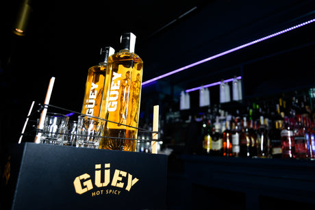 Güey Hot Spicy Tequila, stilvoll präsentiert mit Gläsern in einer Bar-Atmosphäre, beleuchtet von violettem Licht.