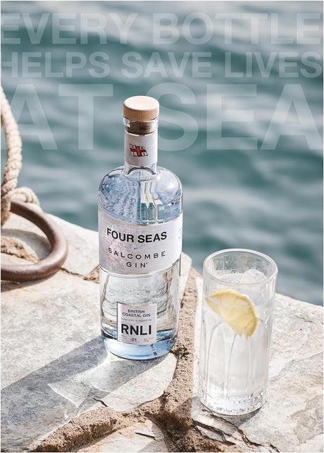 Four Seas Salcombe Gin Flasche am Meer neben Gin Tonic mit Zitronenscheibe auf Steinoberfläche