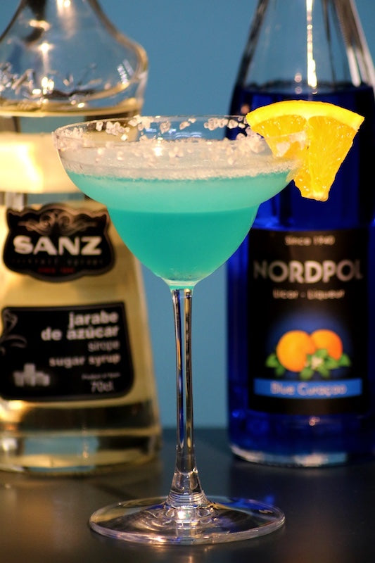 Frozen Blue Daiquiri mit Salzrand und Orangenscheibe, davor Sanz Zuckersirup und Nordpol Blue Curacao Likör.