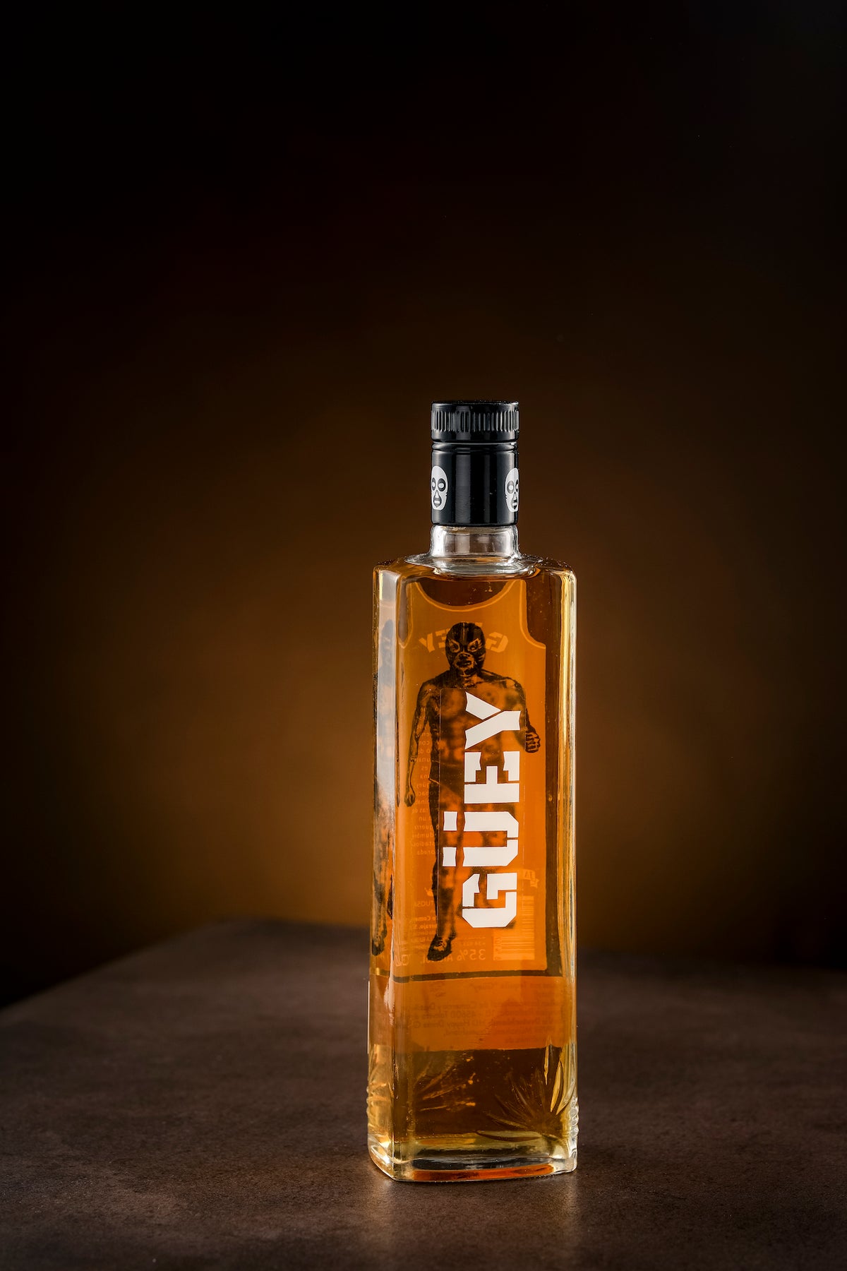 Goldener Tequila Güey in einer eleganten Flasche mit Lucha Libre-Design, präsentiert auf einem dunklen Hintergrund.
