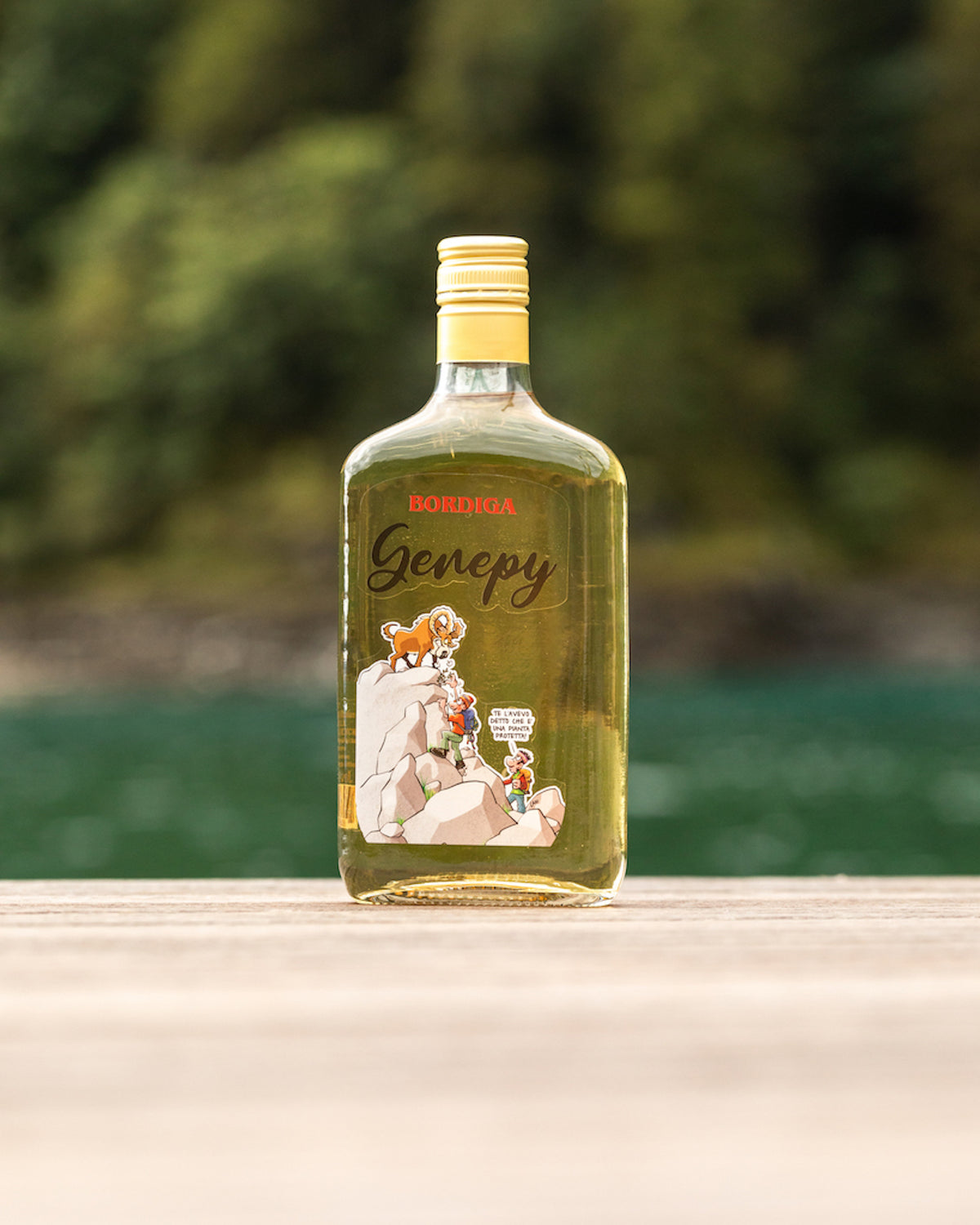 Flasche Bordiga Genepy Likör mit Comic-Illustration auf dem Etikett, stehend auf Holzfläche vor unscharfem Naturhintergrund.