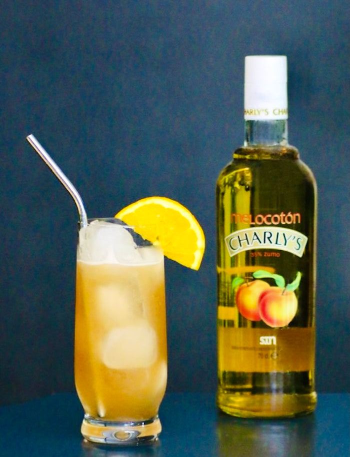 Alkoholfreier Georgia Peach Cocktail mit Eiswürfeln, Orangenscheibe als Garnitur und Charly’s Pfirsich-Flasche im Hintergrund.
